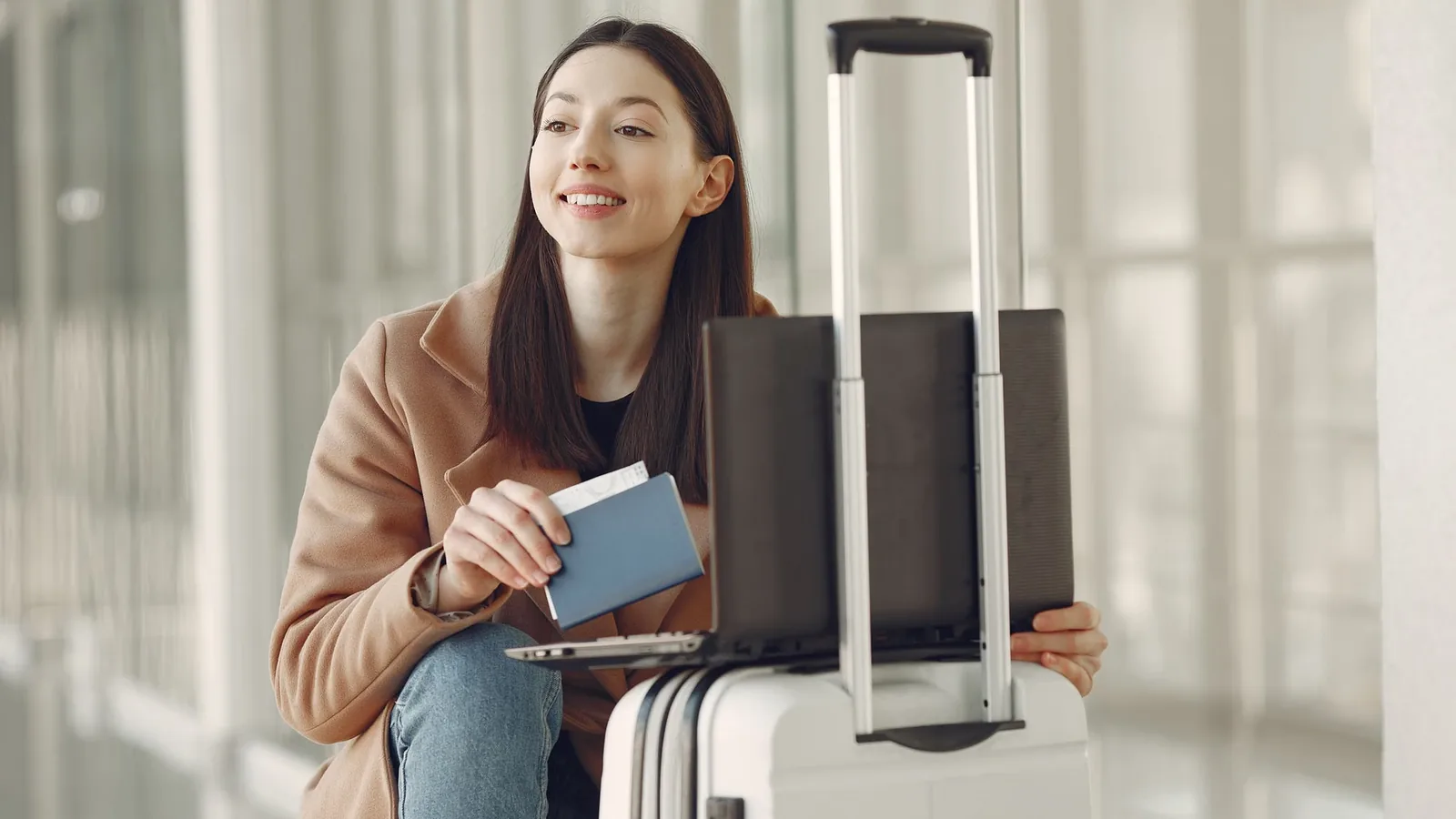 Woman using a laptop with a passport and luggage while waiting in an airport